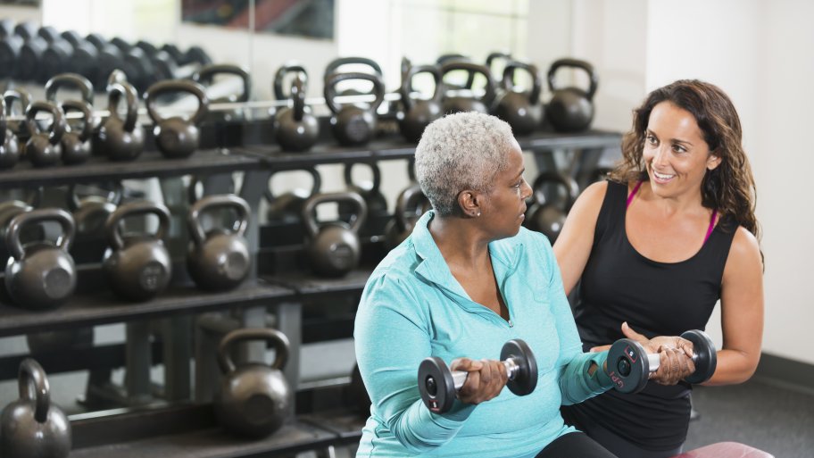 A personal trainer works out with a client in a gym.